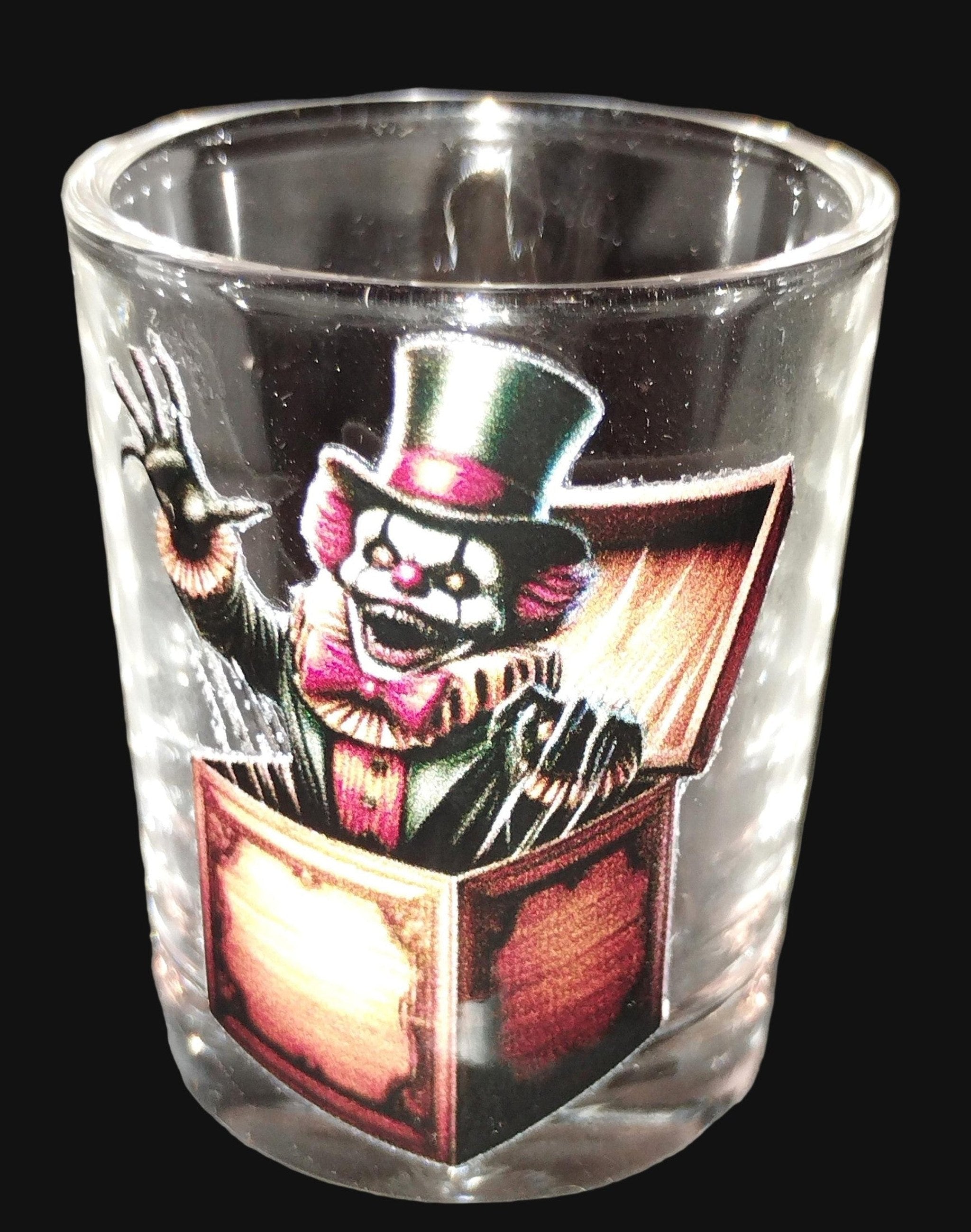 Glass shot glass with a clown design on a dark surface