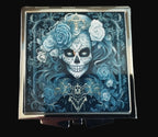 Compact mirror with a skull and floral design on a wooden surface