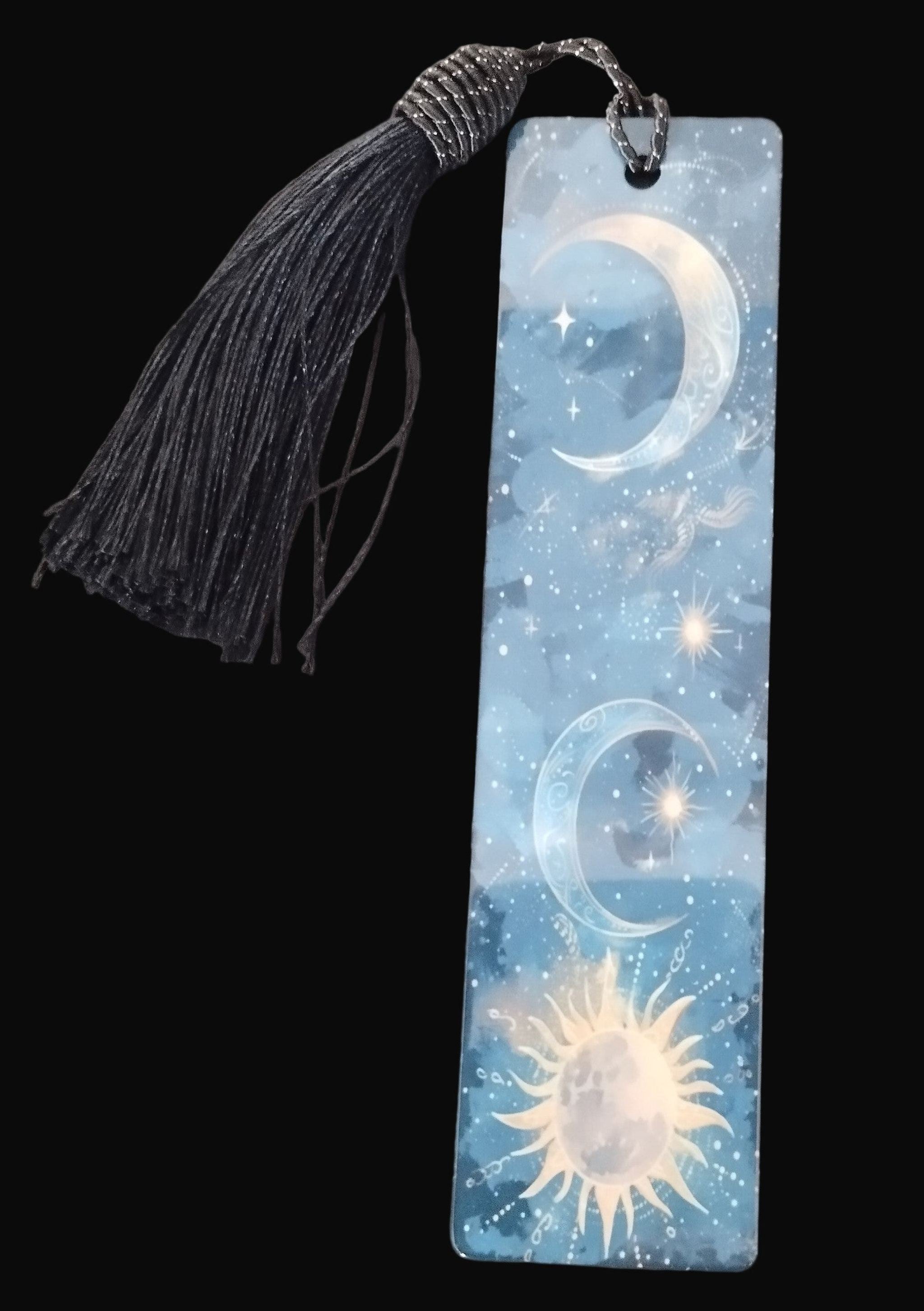 Bookmark with celestial design featuring moon and sun on a blue background, attached to a black tassel.