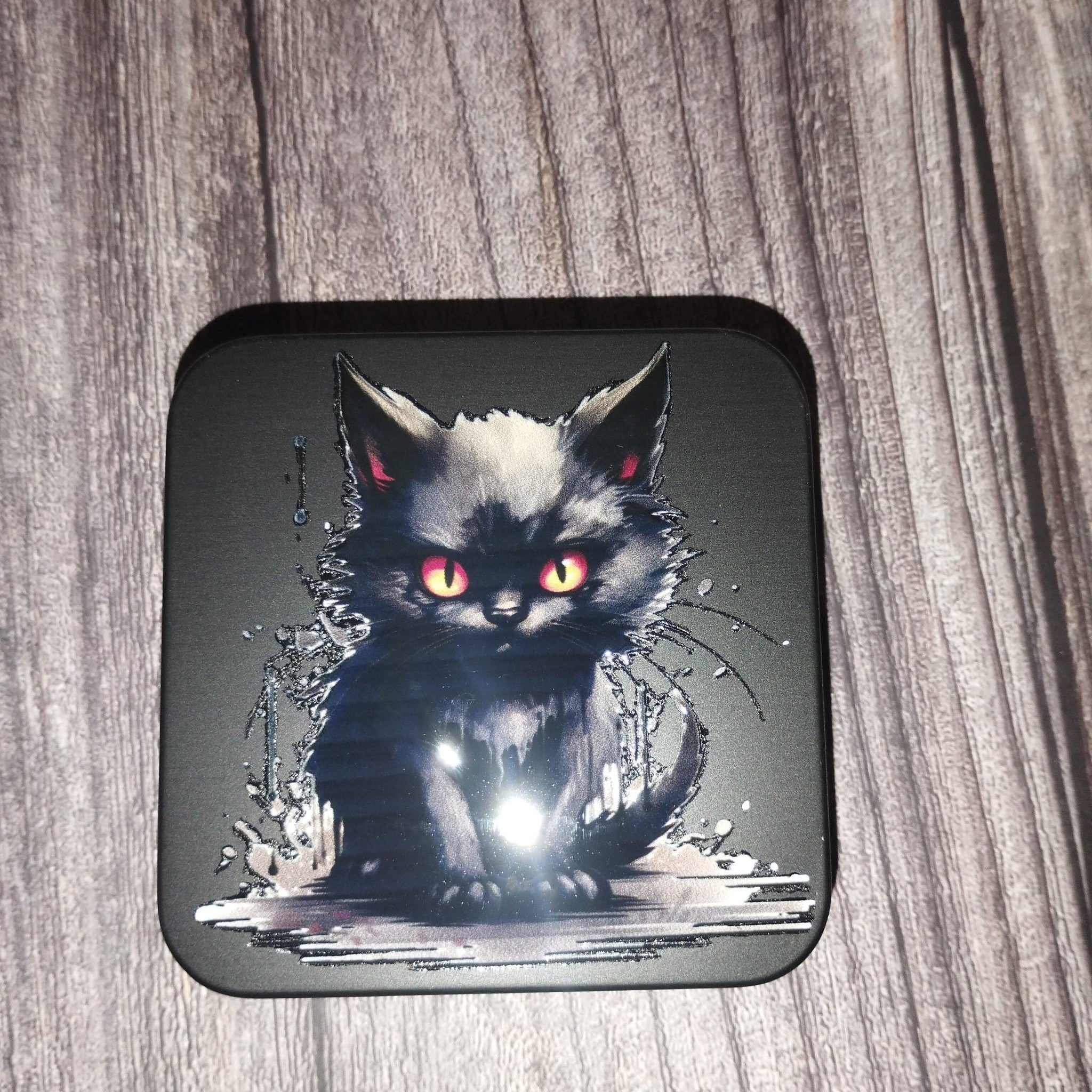 Black cat with red eyes design on a square black tin against a wooden background