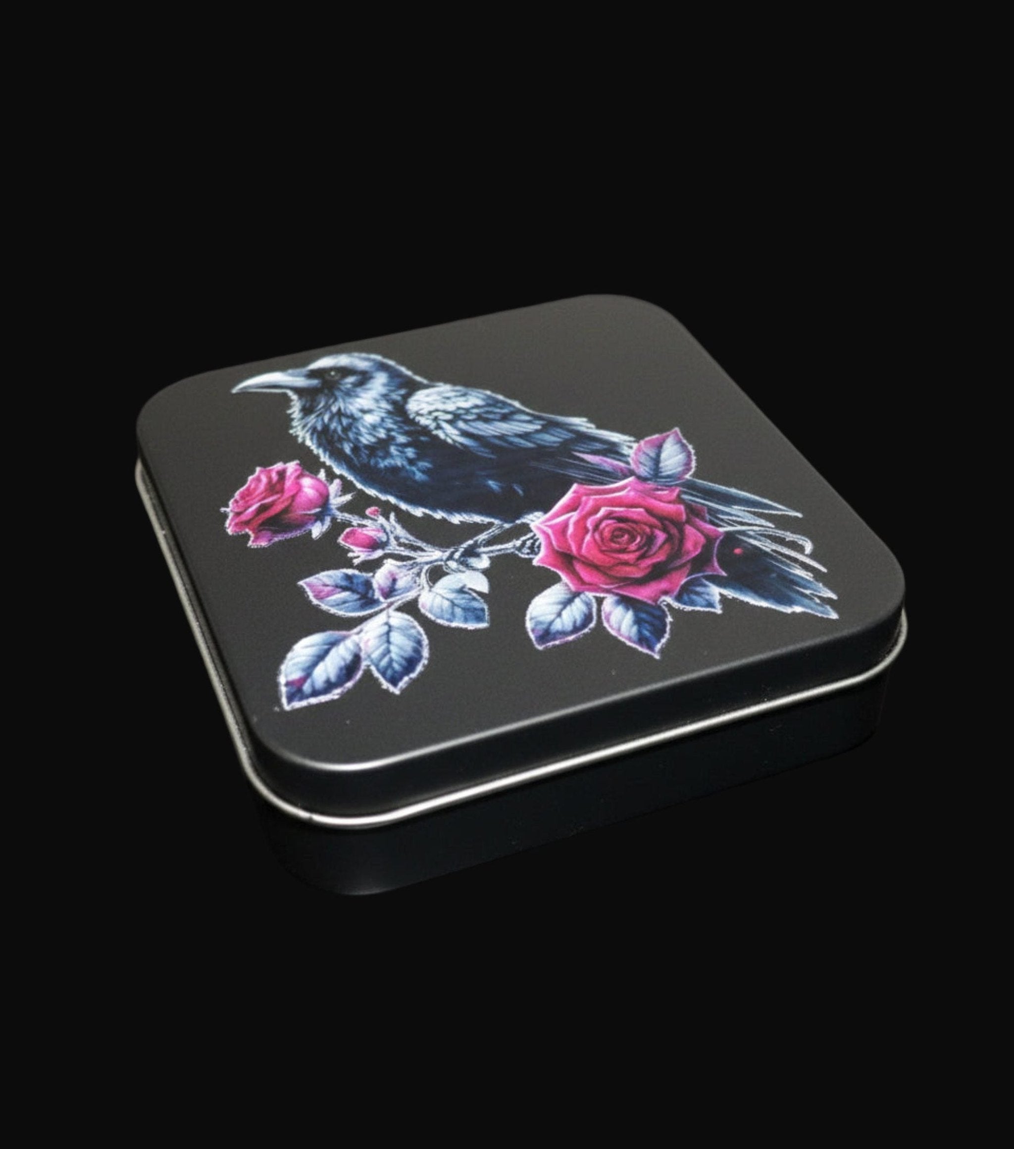 Black tin with a design of a crow and pink roses on a wooden surface
