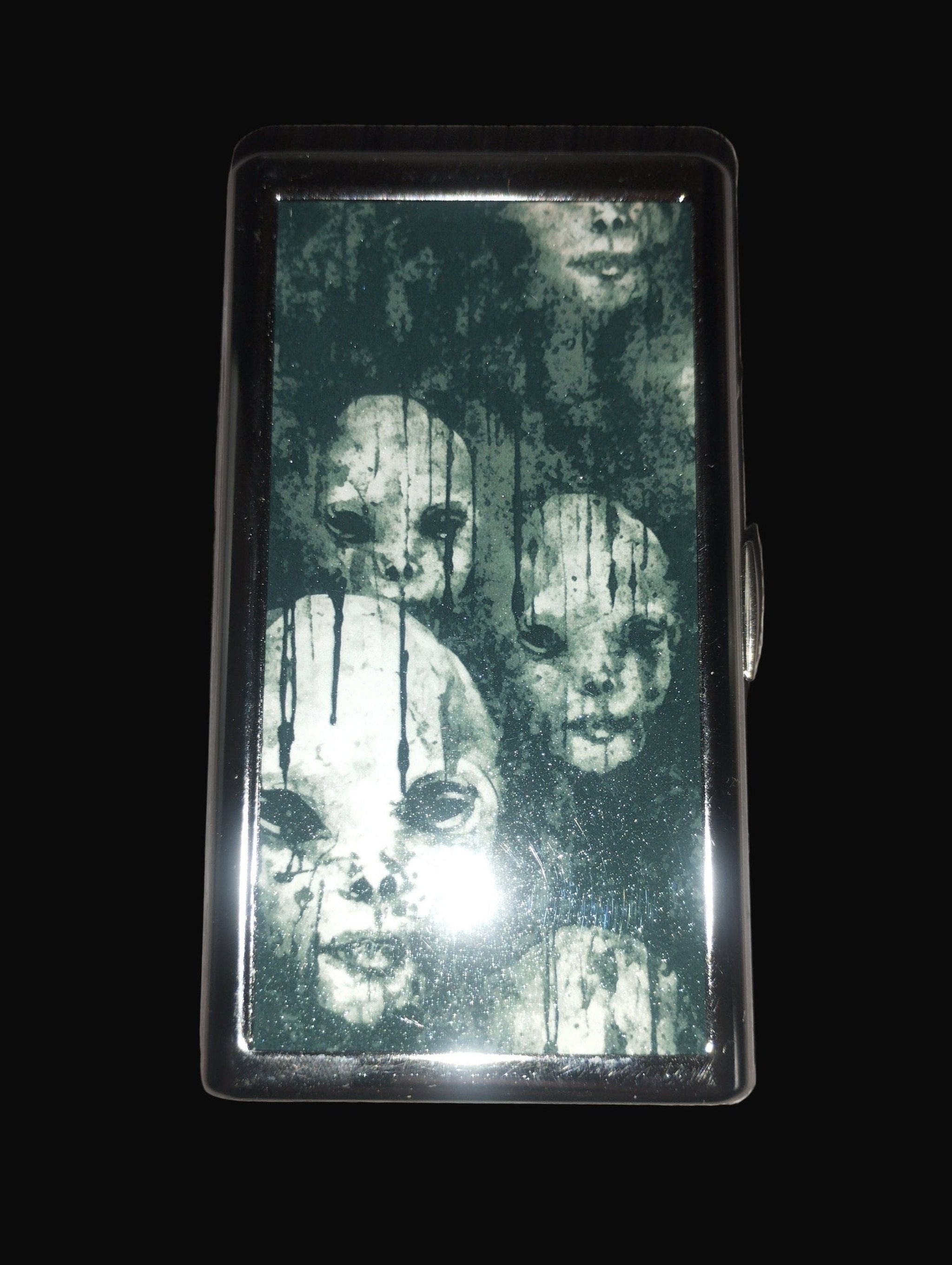 Cigarette case with ghostly faces design on a wooden surface