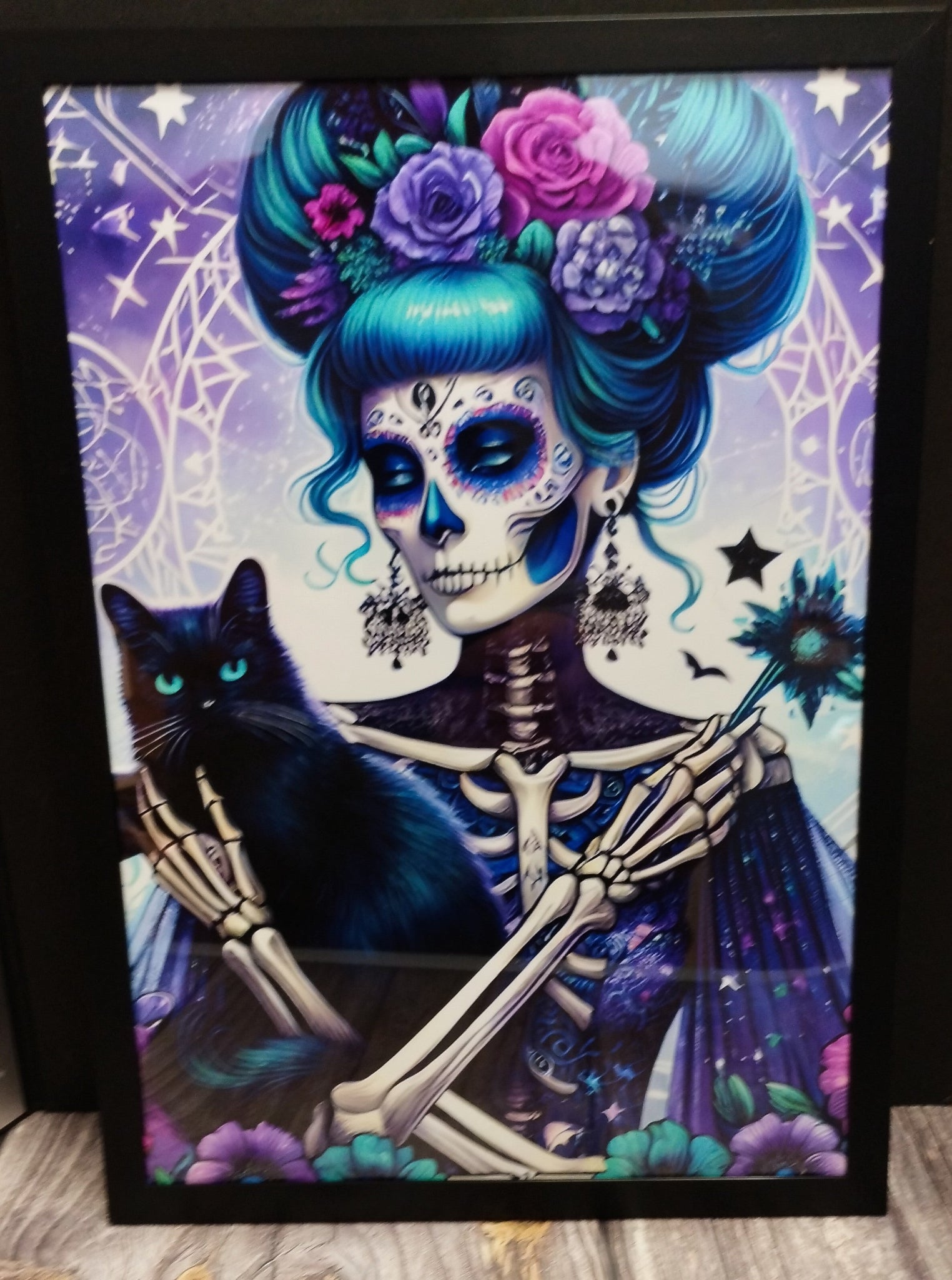 Framed artwork of a skeleton with blue hair and a black cat, set against a purple background with star patterns.
