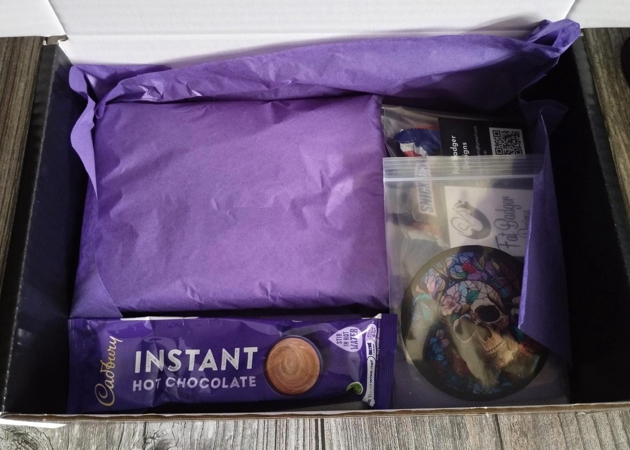 Box containing Cadbury instant hot chocolate mix and a purple fabric item.