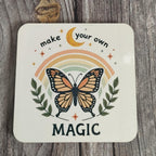 Coasterwith a butterfly, rainbow, and text 'make your own magic' on a wooden surface