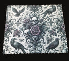 Decorative lens cloth with skull, roses, and crows on a wooden surface