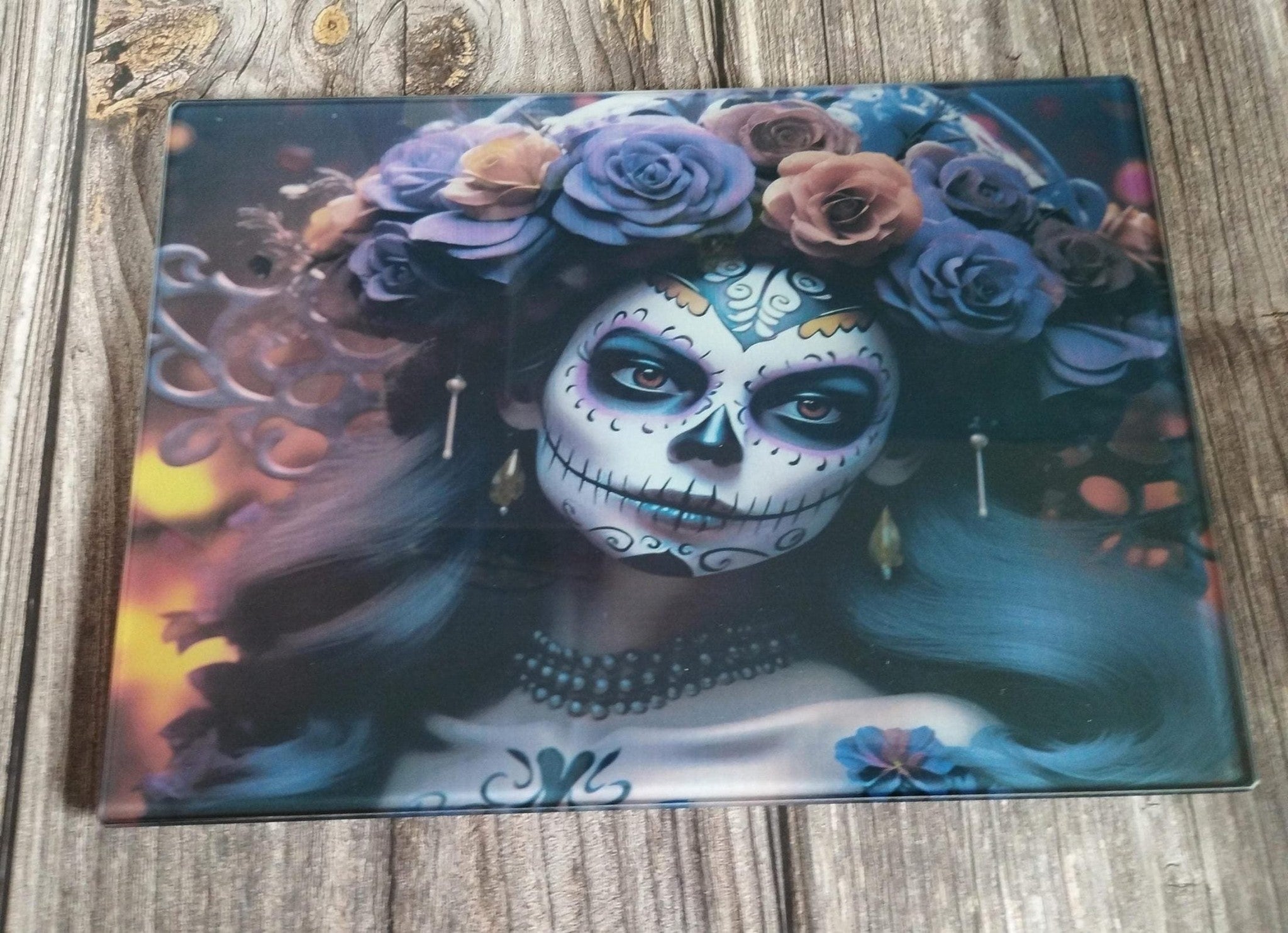 Decorative glass panel with a design of a woman with sugar skull makeup and floral headpiece on a wooden surface.