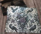 Decorative lens cloth with skull, roses, and crows design on a wooden surface