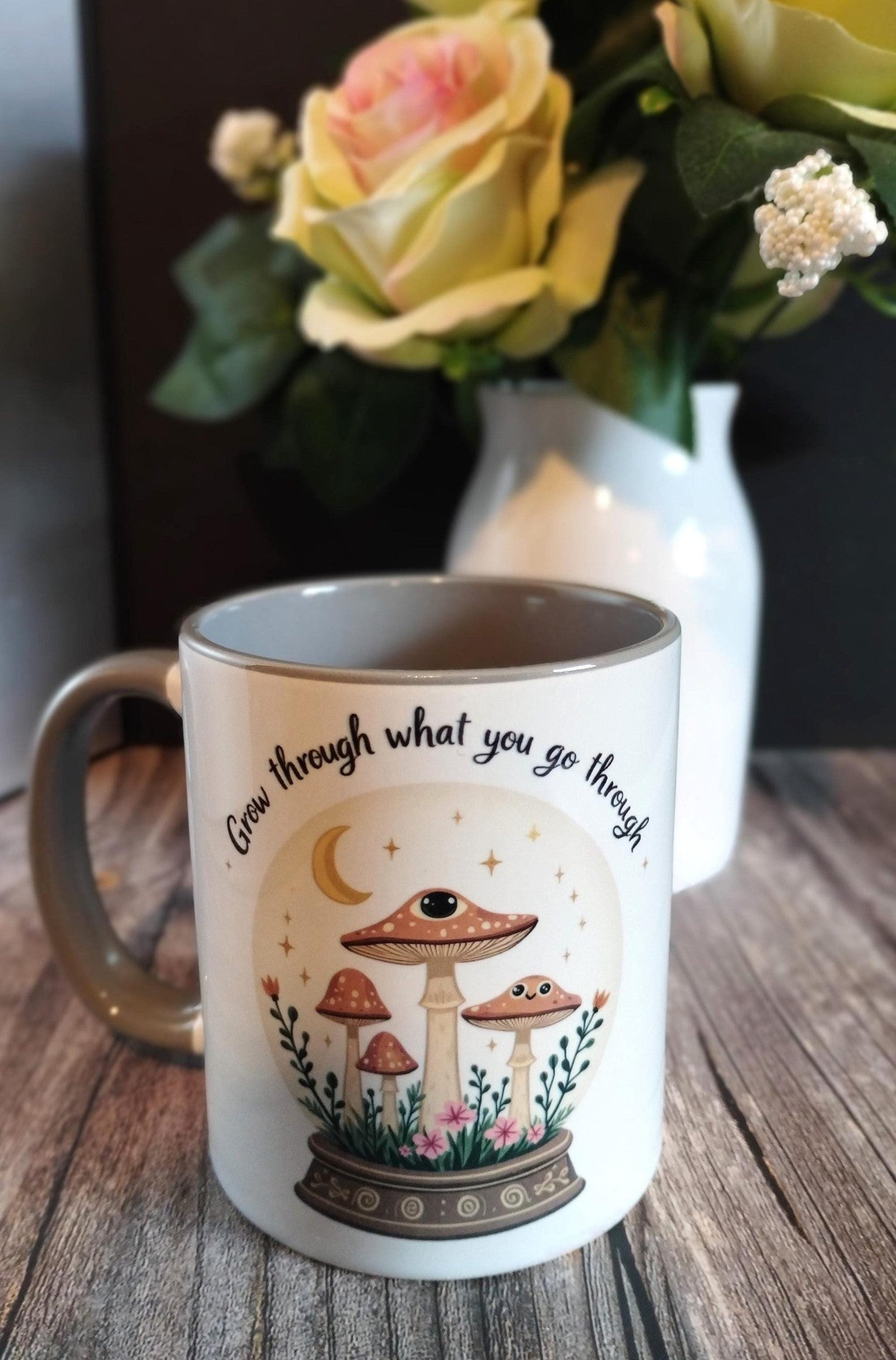 Mug with mushroom design and text on a wooden surface with flowers in the background
