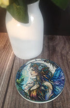 Coaster with a colorful fairy design on a wooden surface next to a white vase.