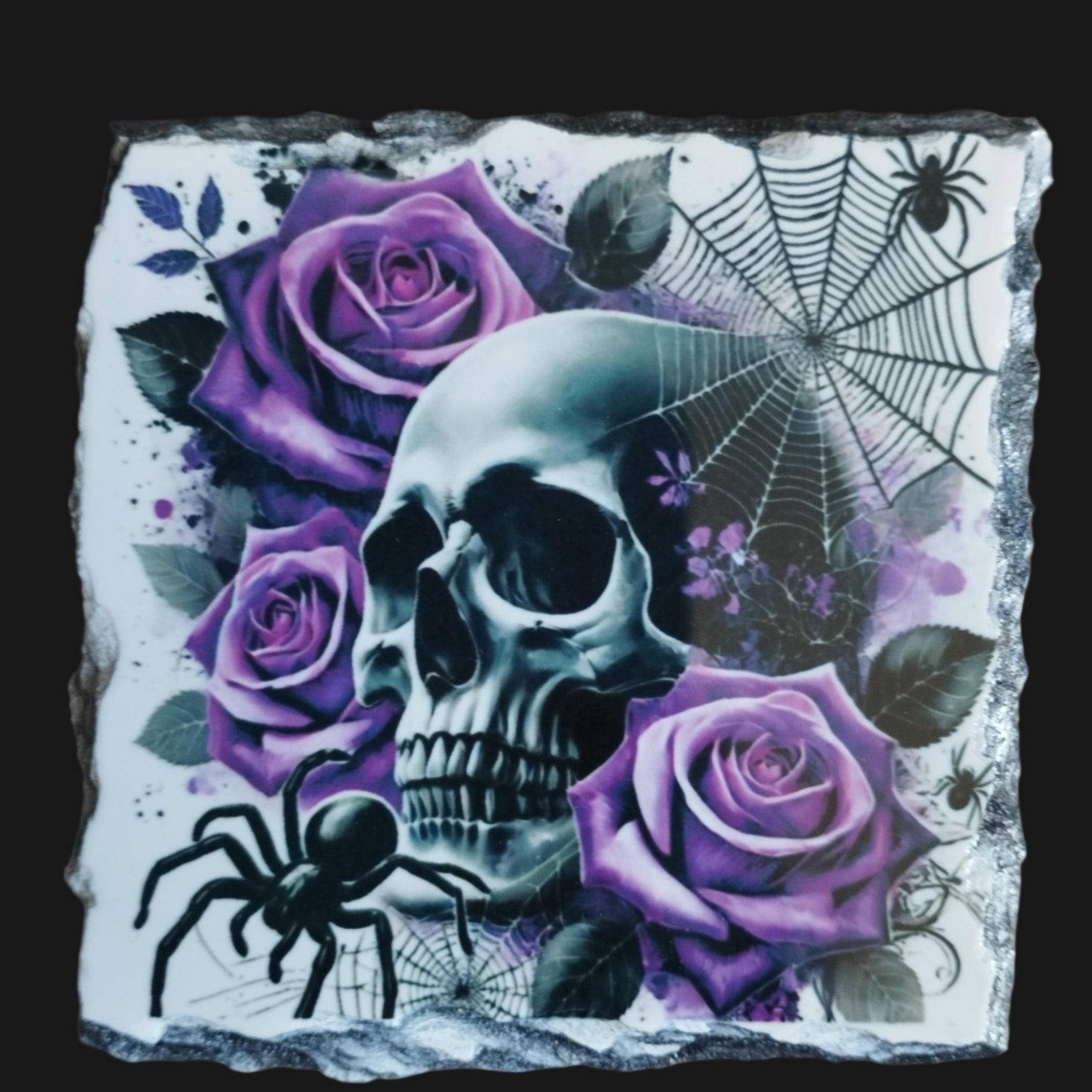Decorative stone with a skull, purple roses, and spiders on a wooden surface