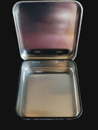 Metallic square tin with lid on a black surface