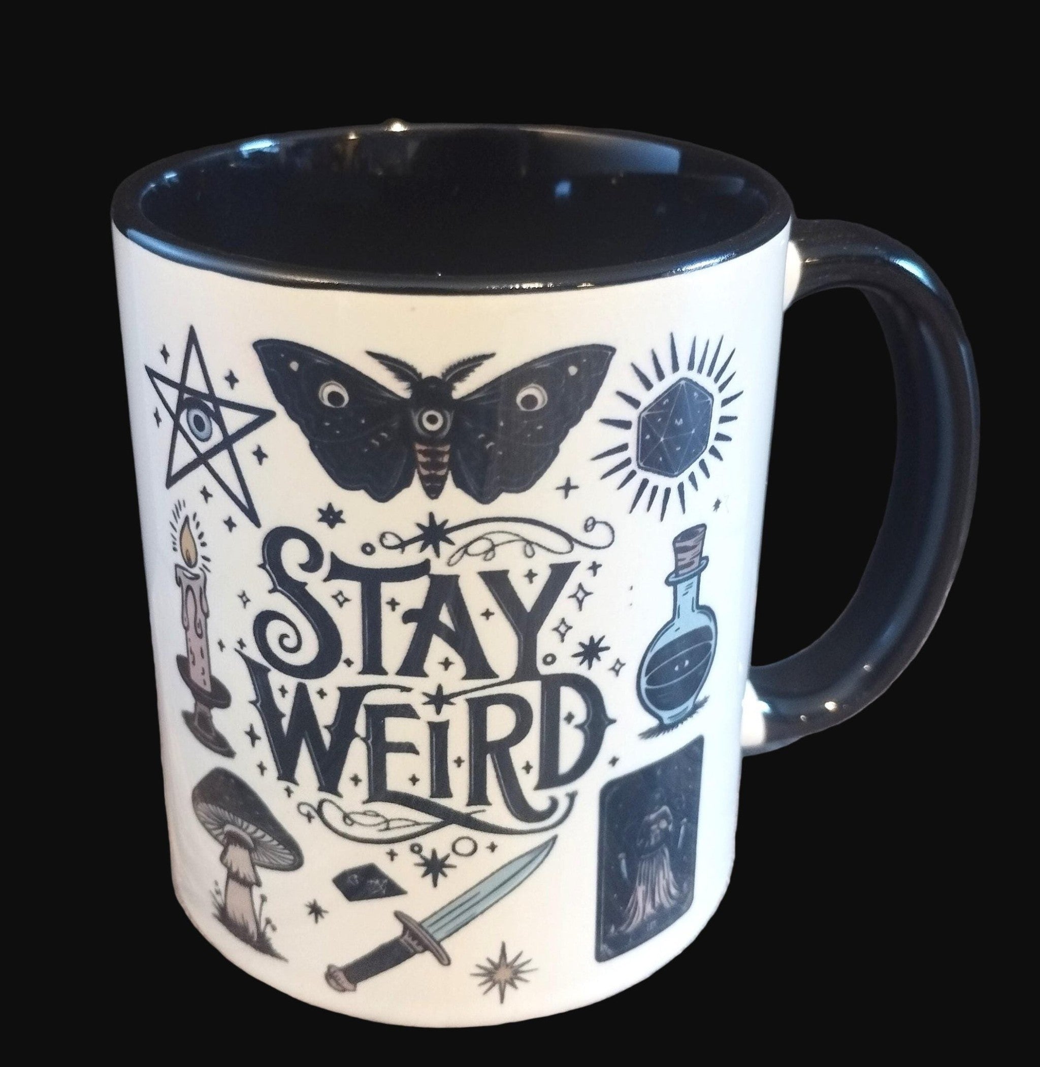 Mug with 'Stay Weird' text and mystical illustrations on a wooden surface.