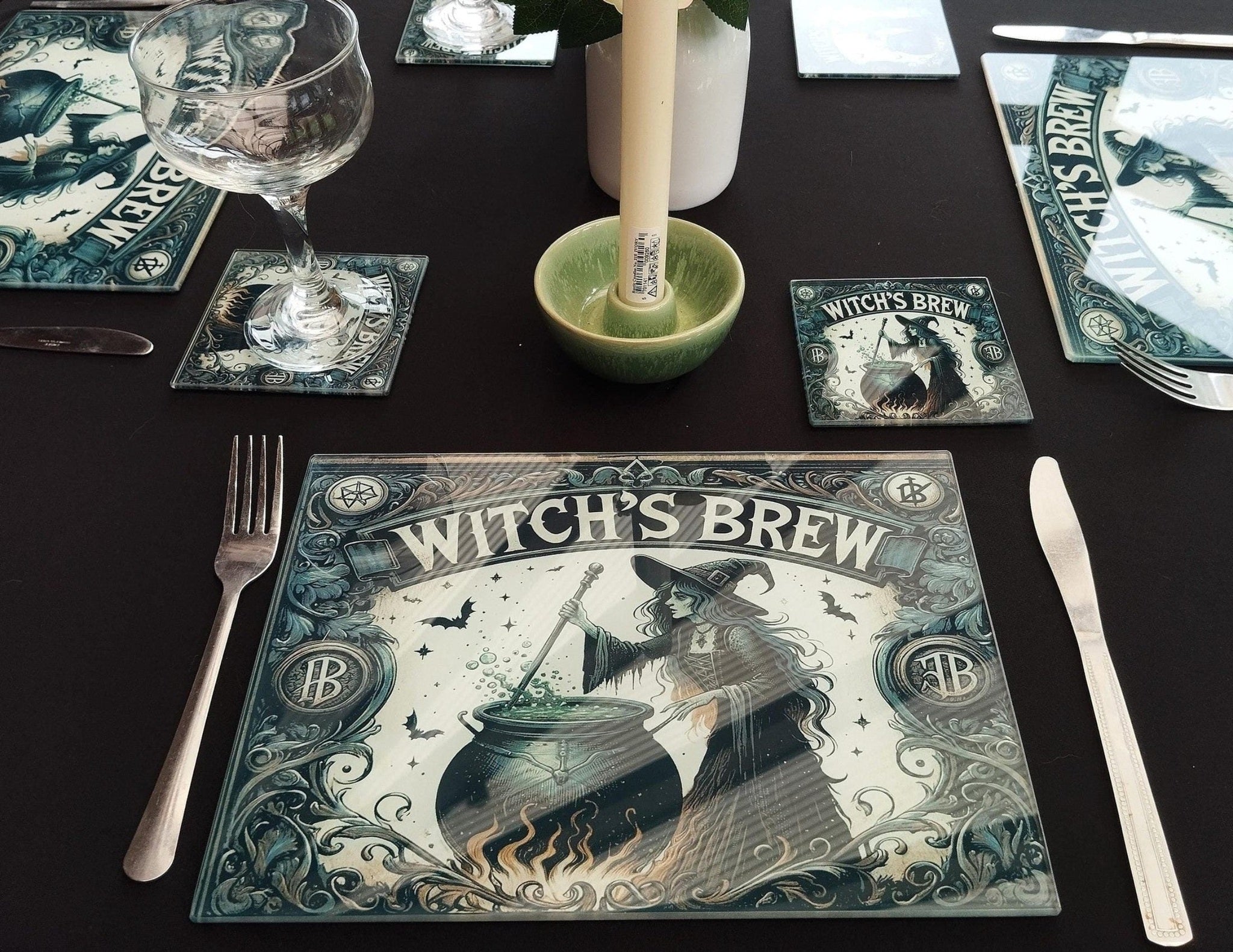 Table setting with 'Witch's Brew' themed placemats, glasses, and cutlery on a black surface.