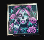 Compact mirror with a colorful design of a sugar skull with pink hair and roses on a wooden surface.