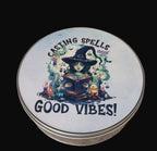 Tin lid with a witch illustration and text 'Casting Spells and Good Vibes!' on a wooden surface.