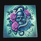 Decorative tile with a skull, snake, and pink roses on a teal background, placed on a wooden surface.