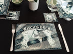 Table setting with 'Witch's Brew' themed placemat, glasses, and cutlery on a black surface.