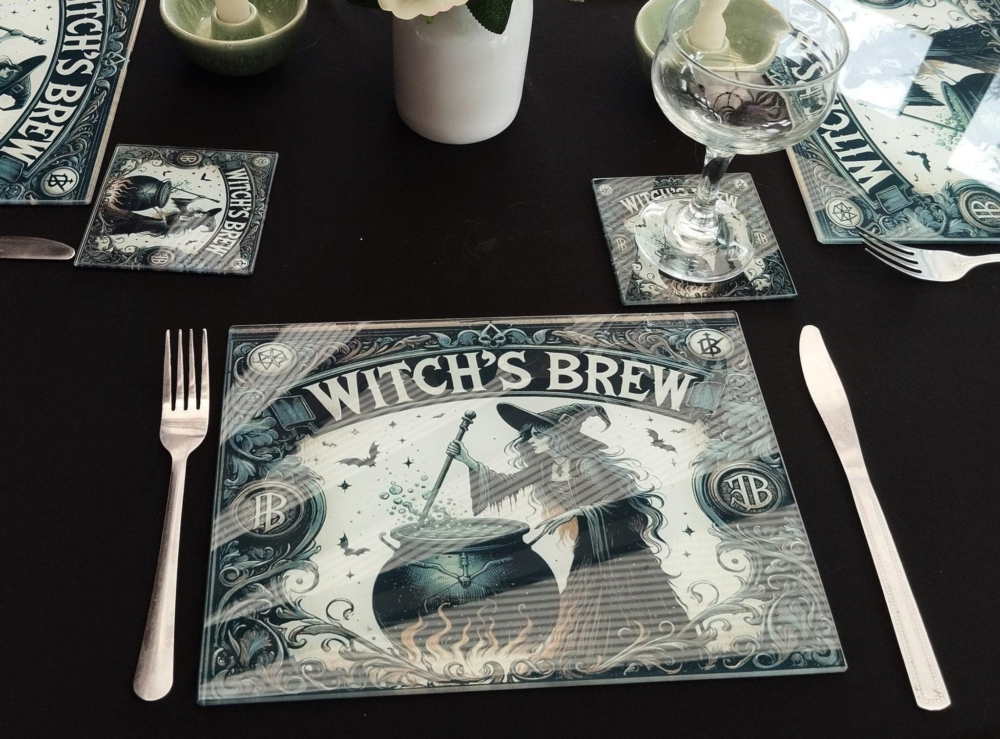 Table setting with 'Witch's Brew' themed placemat, glasses, and cutlery on a black surface.