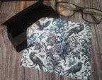 Gothic-themed fabric with raven and skull design on a wooden surface with glasses and black box.