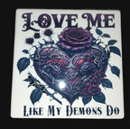 Decorative tile with heart design, roses, and text 'Love me like my demons do' on a wooden surface.