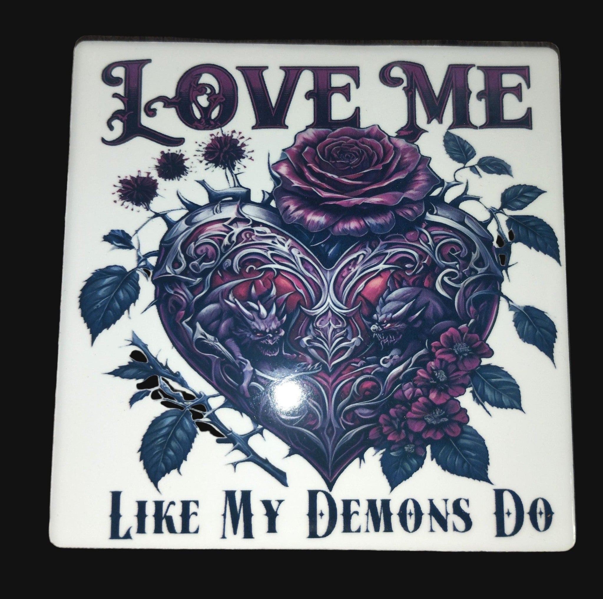 Decorative tile with heart design, roses, and text 'Love me like my demons do' on a wooden surface.
