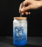 Glass tumbler with capricorn design and wooden lid being held by a hand against a black background