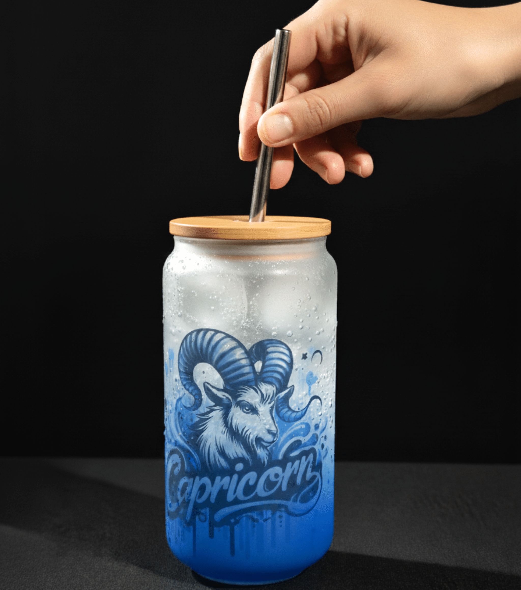 Glass tumbler with capricorn design and wooden lid being held by a hand against a black background