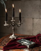 Candlelit scene with a silver candelabra, books, and a red cloth on a wooden surface.