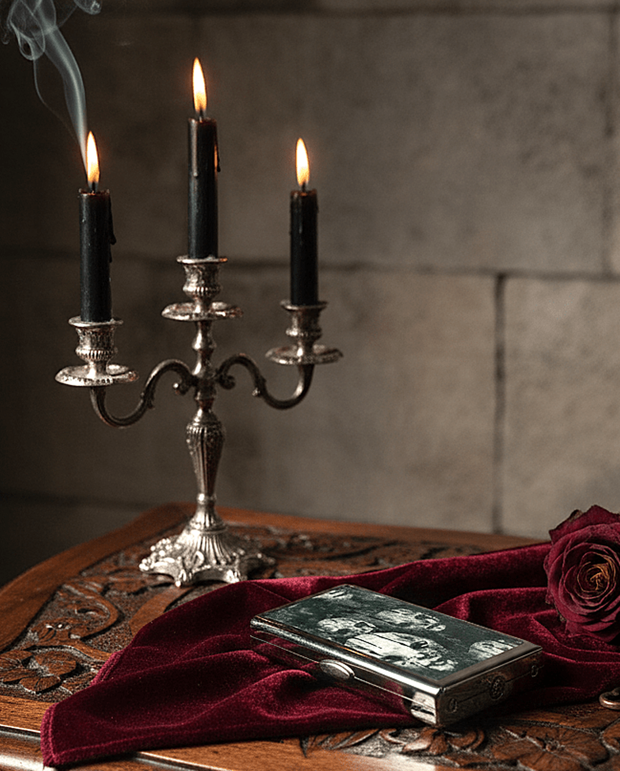 Candlelit scene with a silver candelabra, books, and a red cloth on a wooden surface.