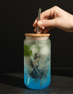 Hand holding a straw over a blue jar with a fairy design on a dark background