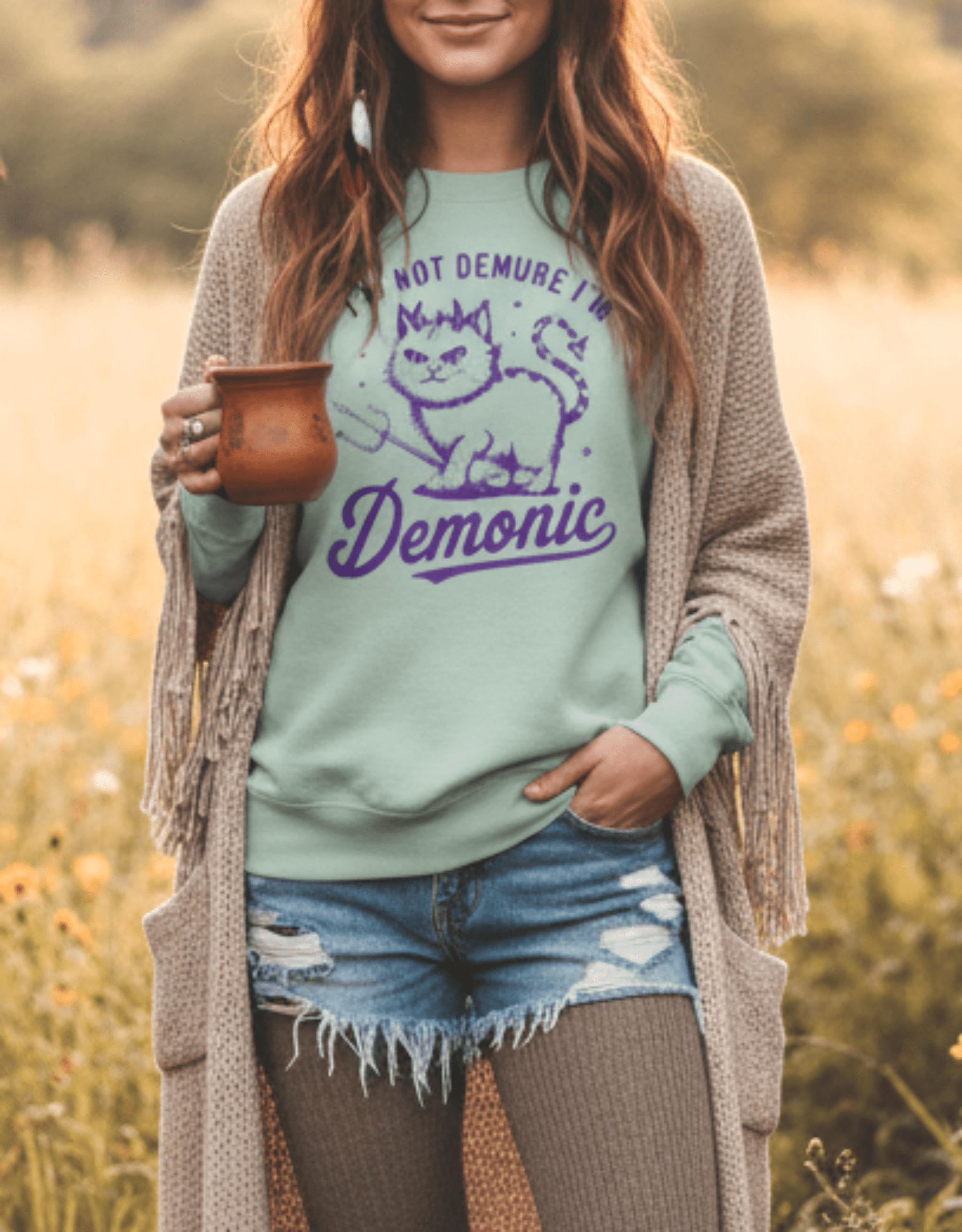 Person wearing a green sweatshirt with a cat graphic and text, standing in a field.