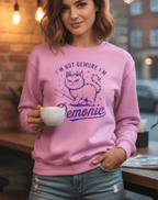 Woman wearing a pink sweatshirt with a cat graphic and text, holding a coffee cup in a casual setting.