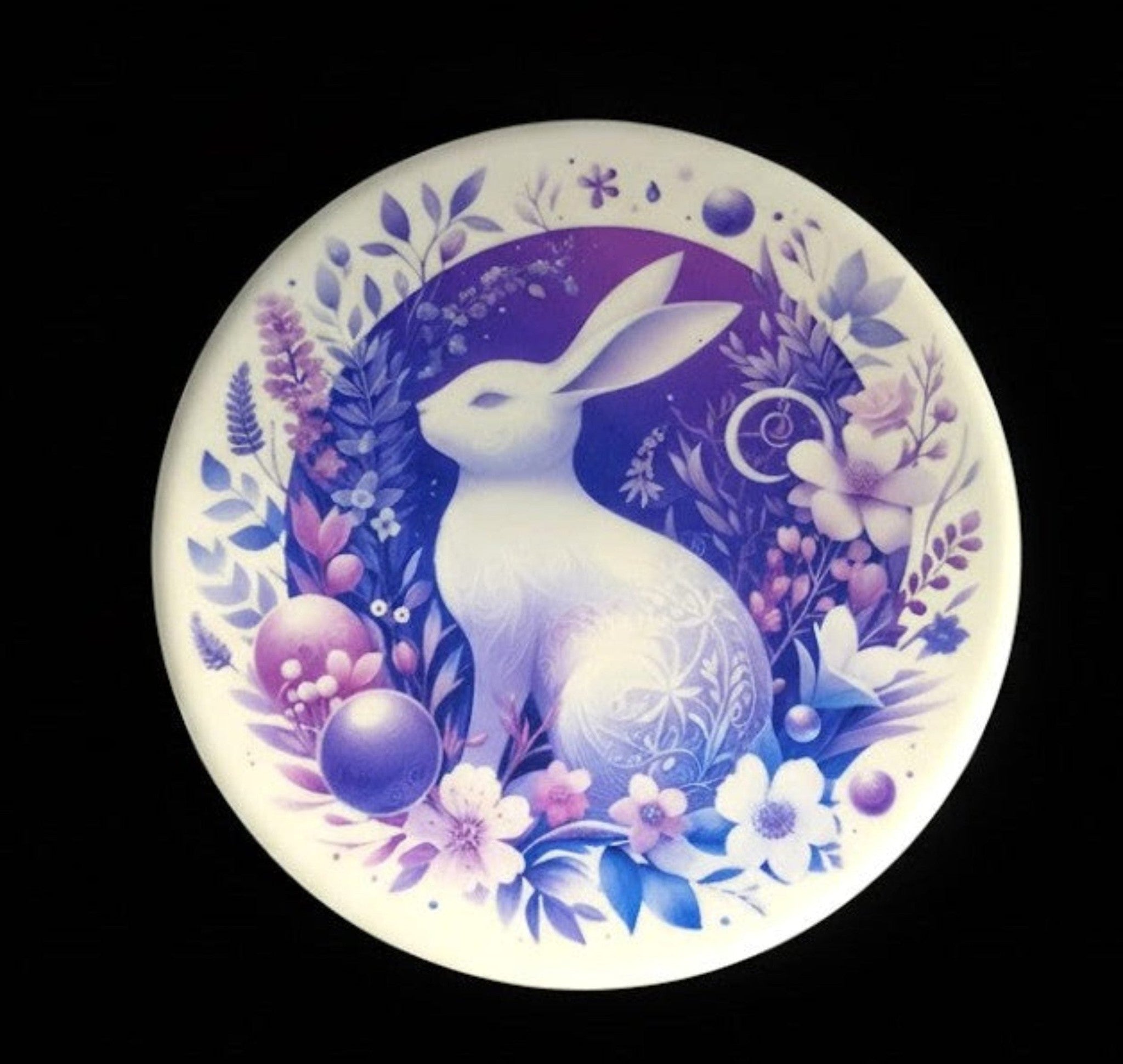 Decorative coaster with a white hare surrounded by flowers and leaves on a black background