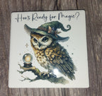 Coaster with an owl wearing a witch hat and crystal ball, text 'Hoo's Ready for Magic?' on a wooden surface.