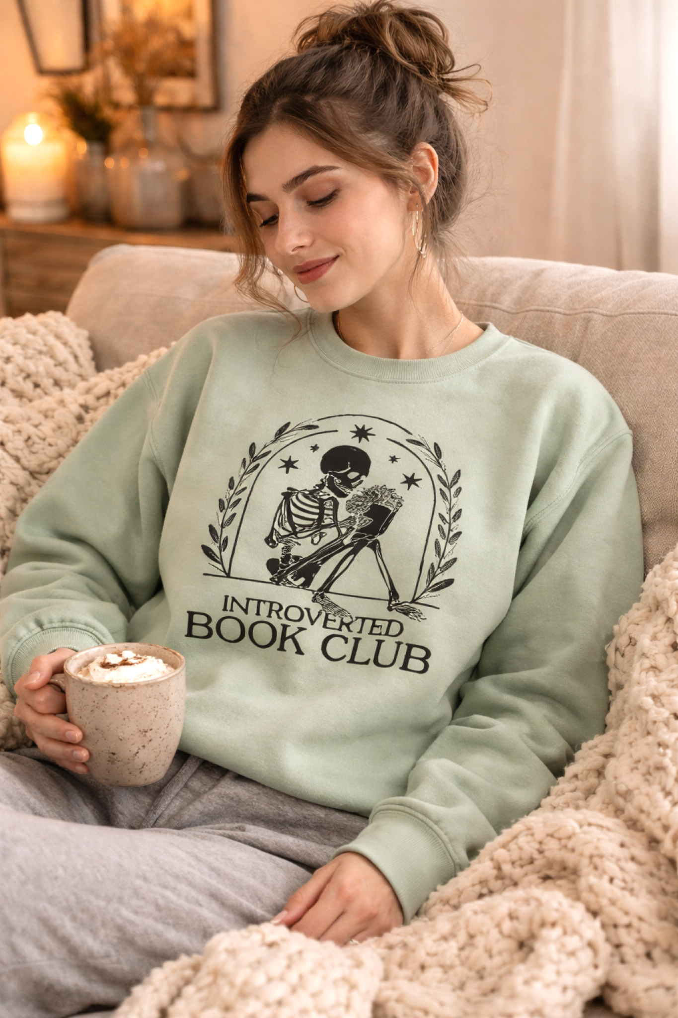 Woman wearing a 'Introverted Book Club' sweatshirt, sitting on a couch with a mug.