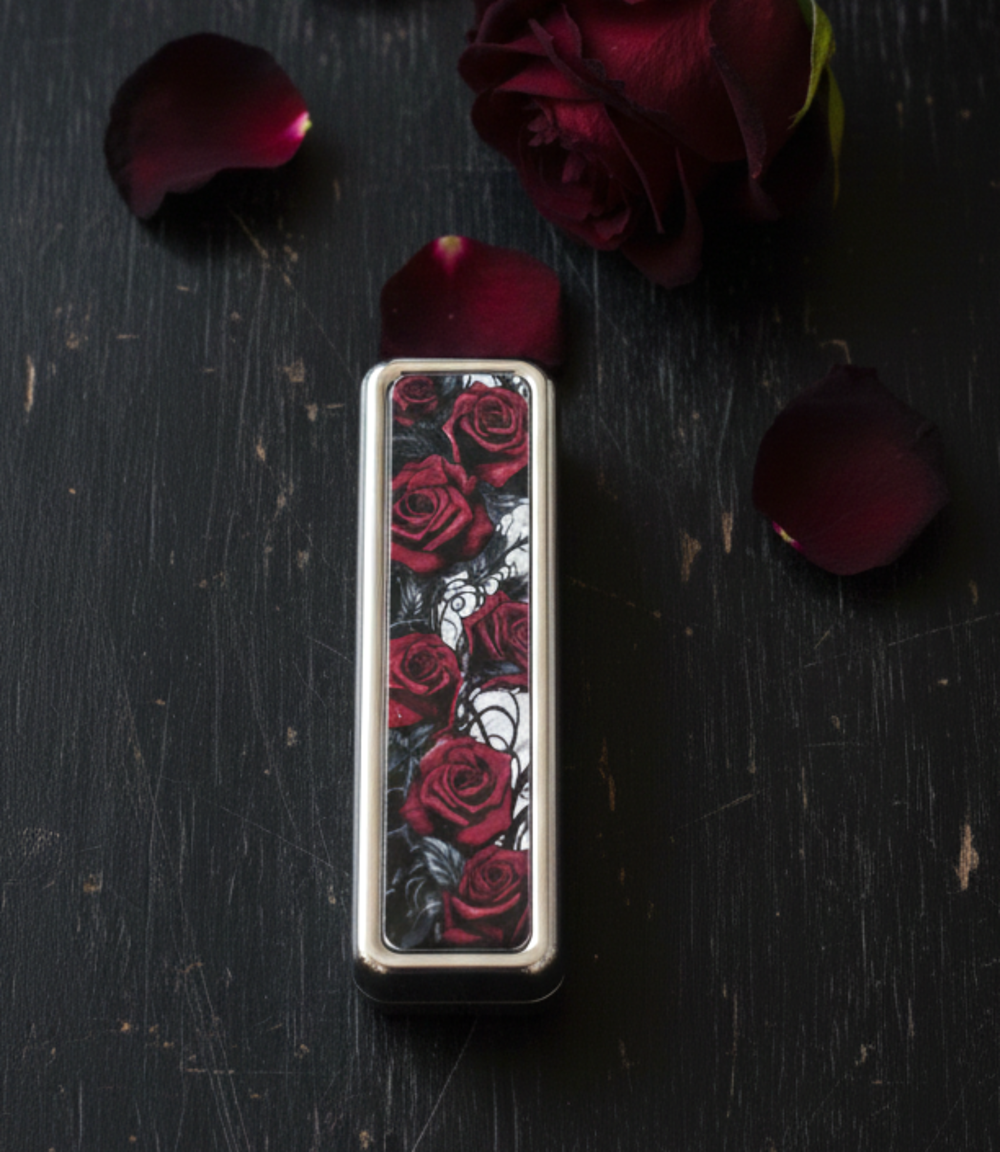 Rectangular object with rose pattern on a dark surface with red roses and petals.