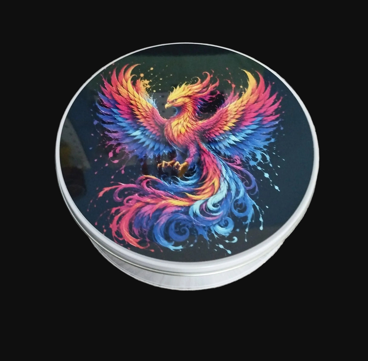 Round silver-coloured metal storage tin with a colourful phoenix design on the lid, on a wooden background.