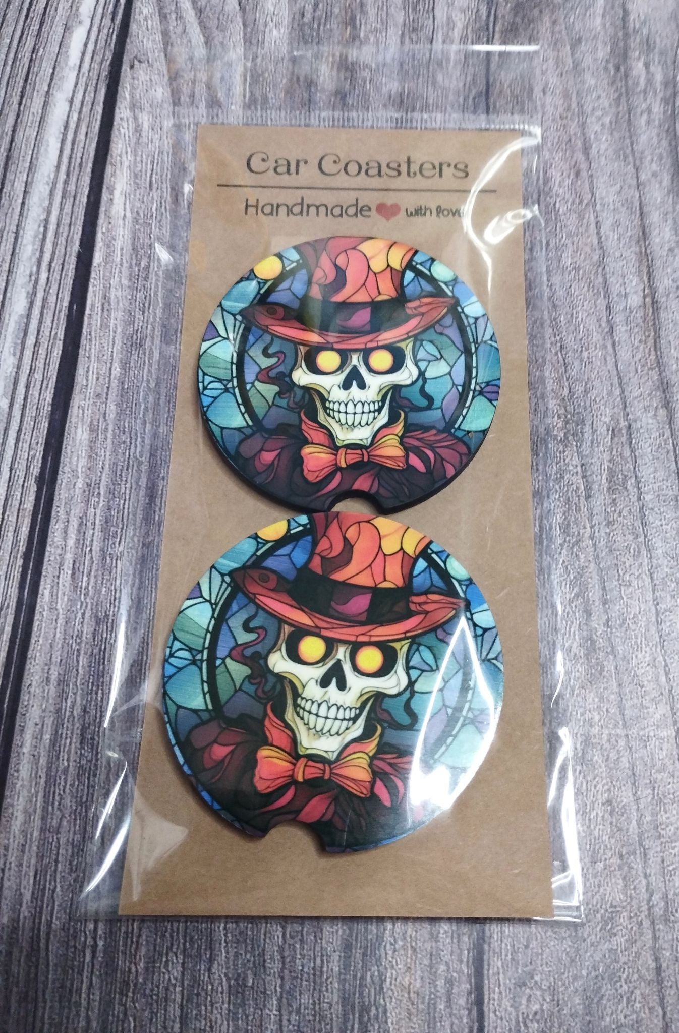 Car coasters with skull design in colorful hats and bow ties, packaged on a wooden surface.
