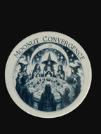 Circular sticker with 'Moonlit Convergence' design featuring witches around a table on a wooden background.