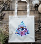 Tote bag with a colorful eye design on a wooden surface with plants.