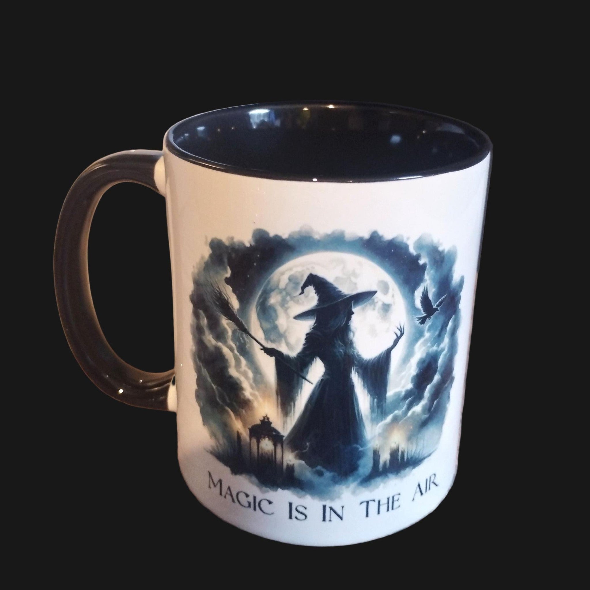 Mug with witch design and 'Magic is in the Air' text on a wooden surface with a vase of flowers in the background.