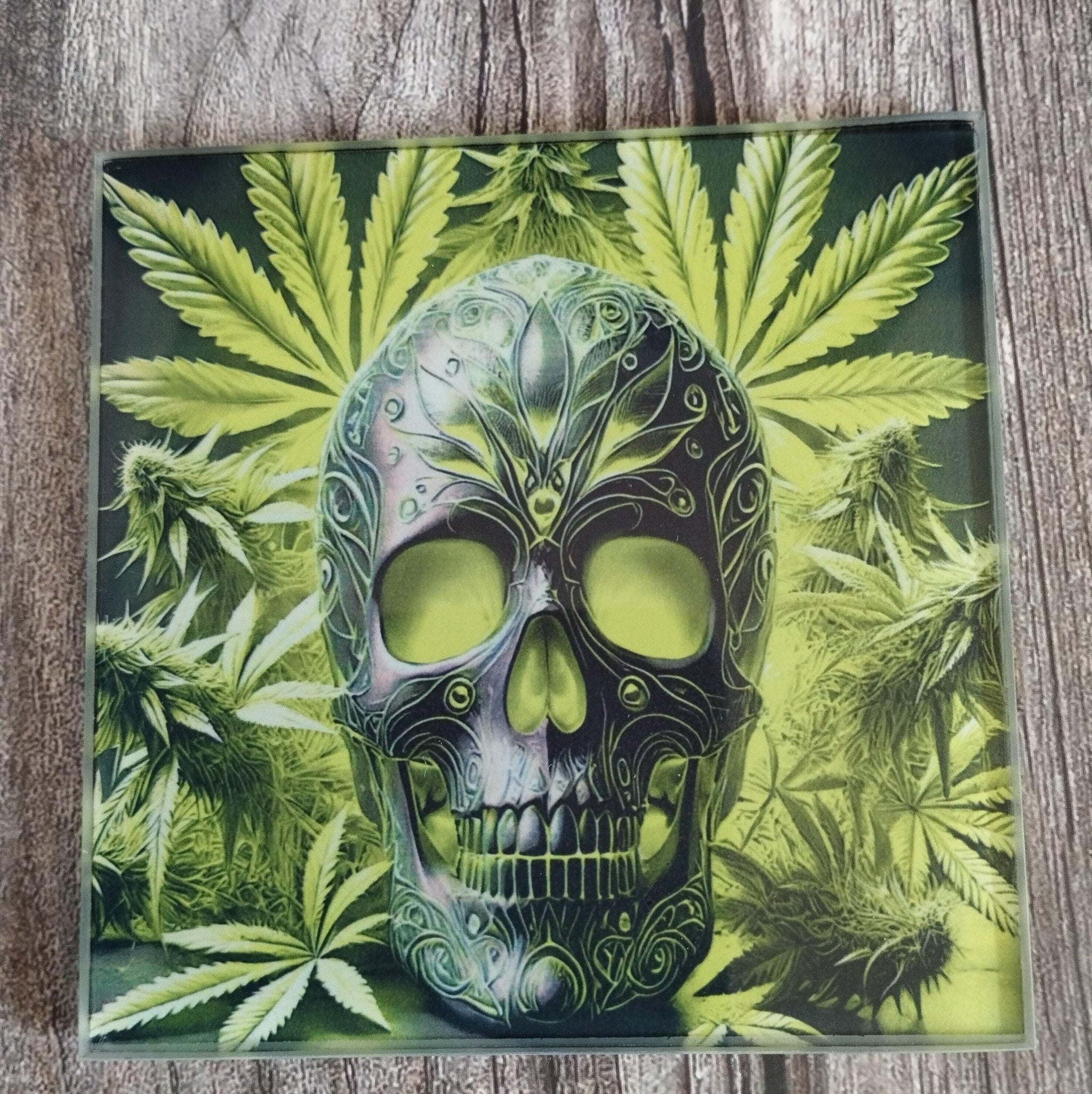 Decorative tile with a skull design and cannabis leaves on a wooden surface