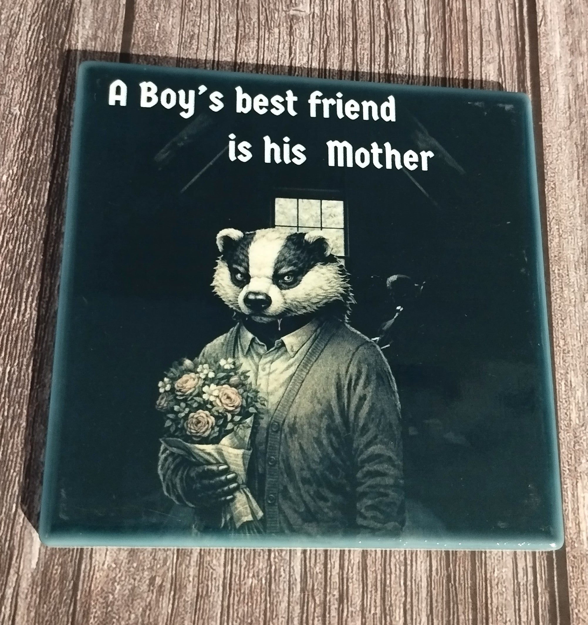Coaster with a badger holding flowers and text 'A Boy's best friend is his Mother' on a wooden surface