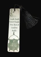 Bookmark with tassel featuring a cauldron design and text on a wooden surface