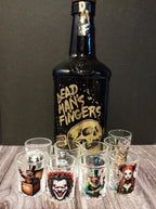 Bottle of 'Dead Man's Fingers' rum with six shot glasses featuring different designs on a wooden surface.