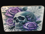Decorative tin with skull, purple roses, and spider web design on a wooden surface.