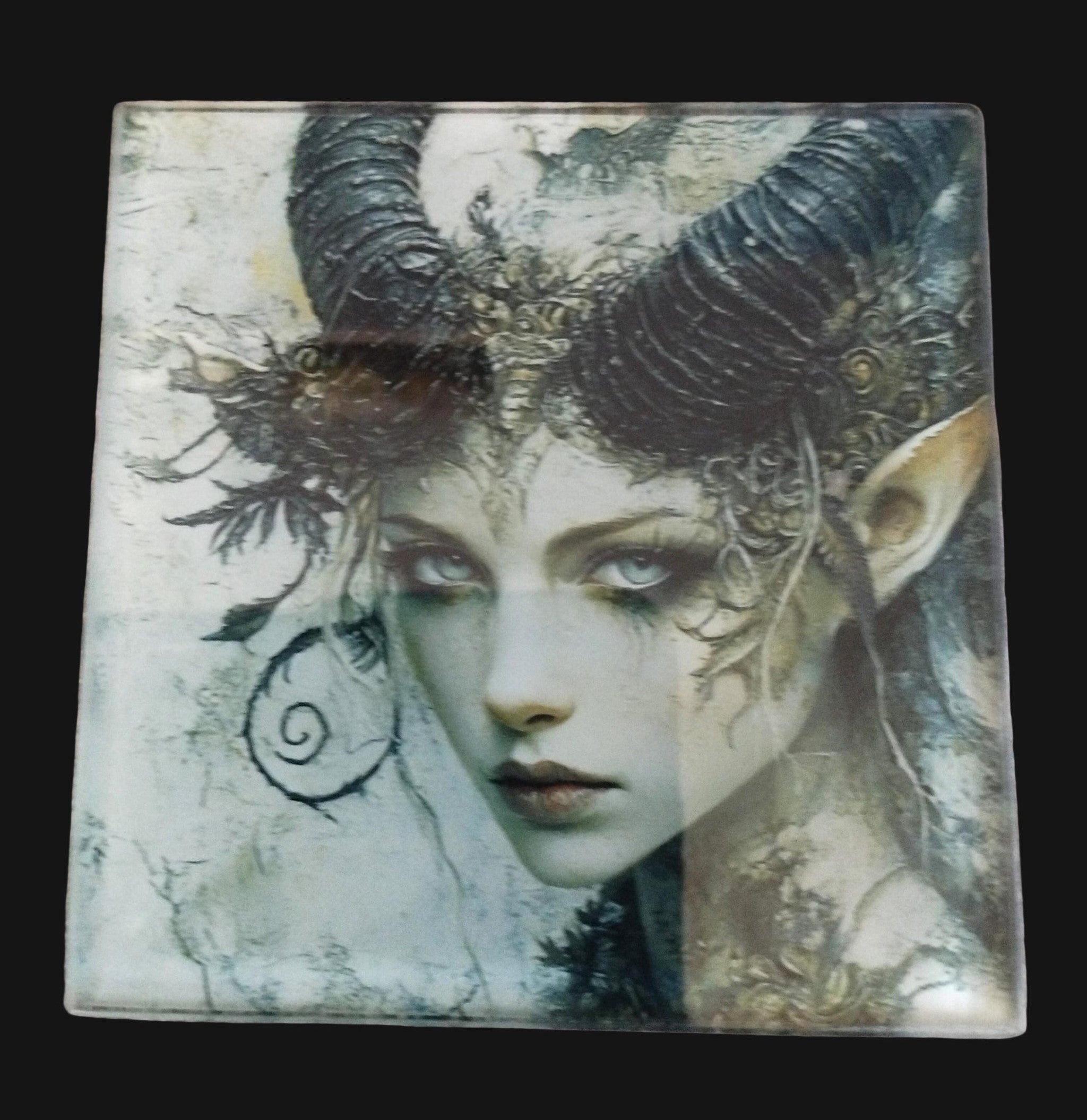 Decorative tile with fantasy-themed design of a creature with horns and elven features on a wooden surface.