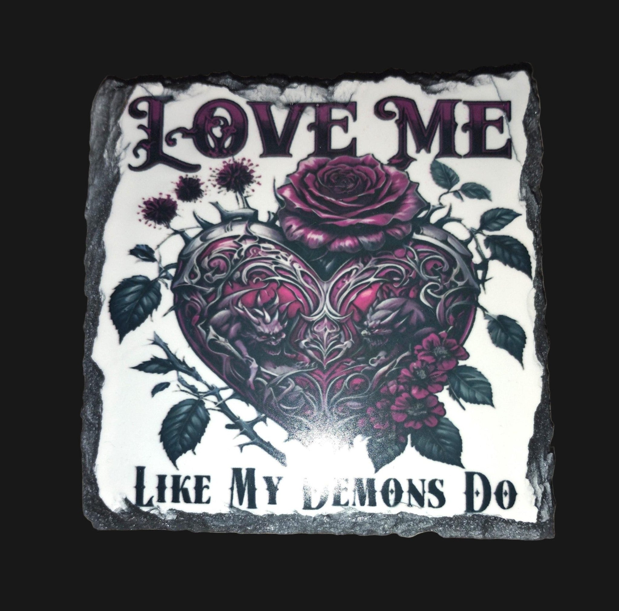 Decorative stone with heart and rose design and text 'Love me like my demons do' on a wooden surface.