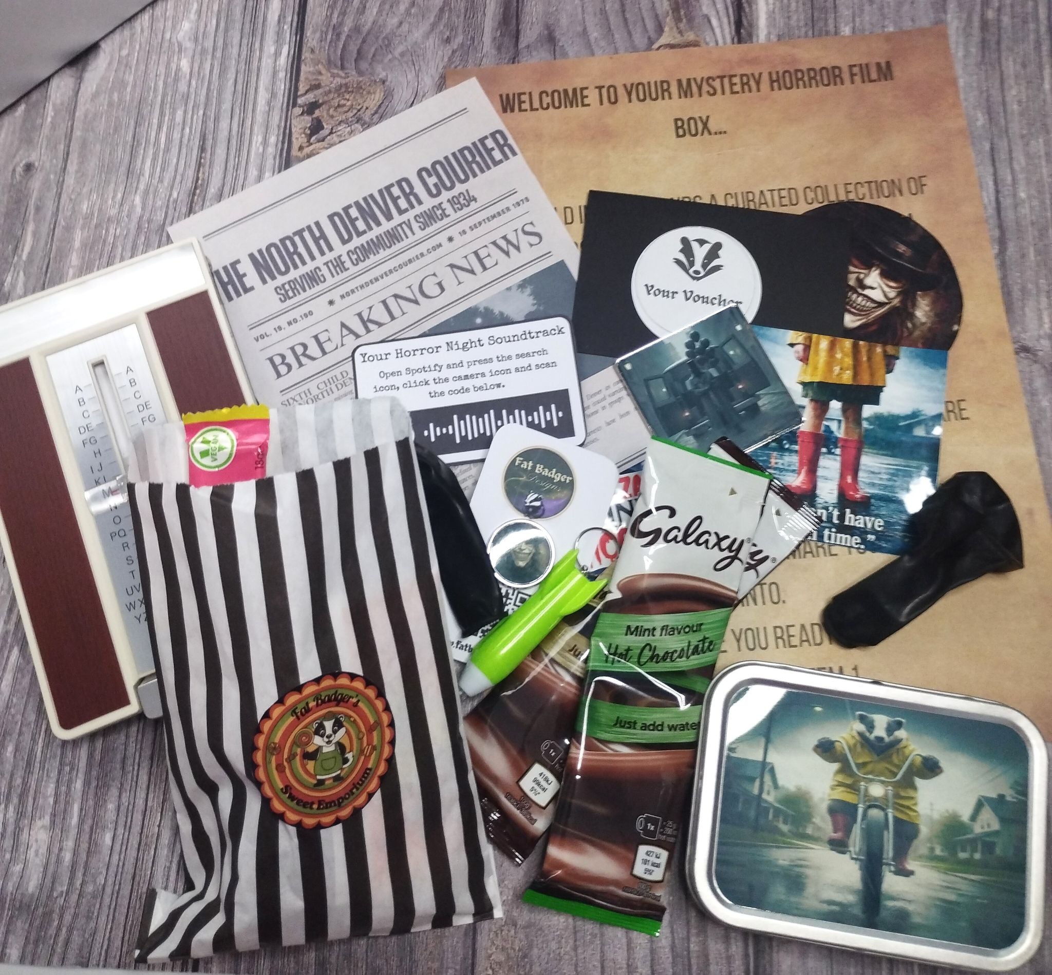 Mystery horror film box with various items including a newspaper, snacks, and a striped bag on a wooden surface.